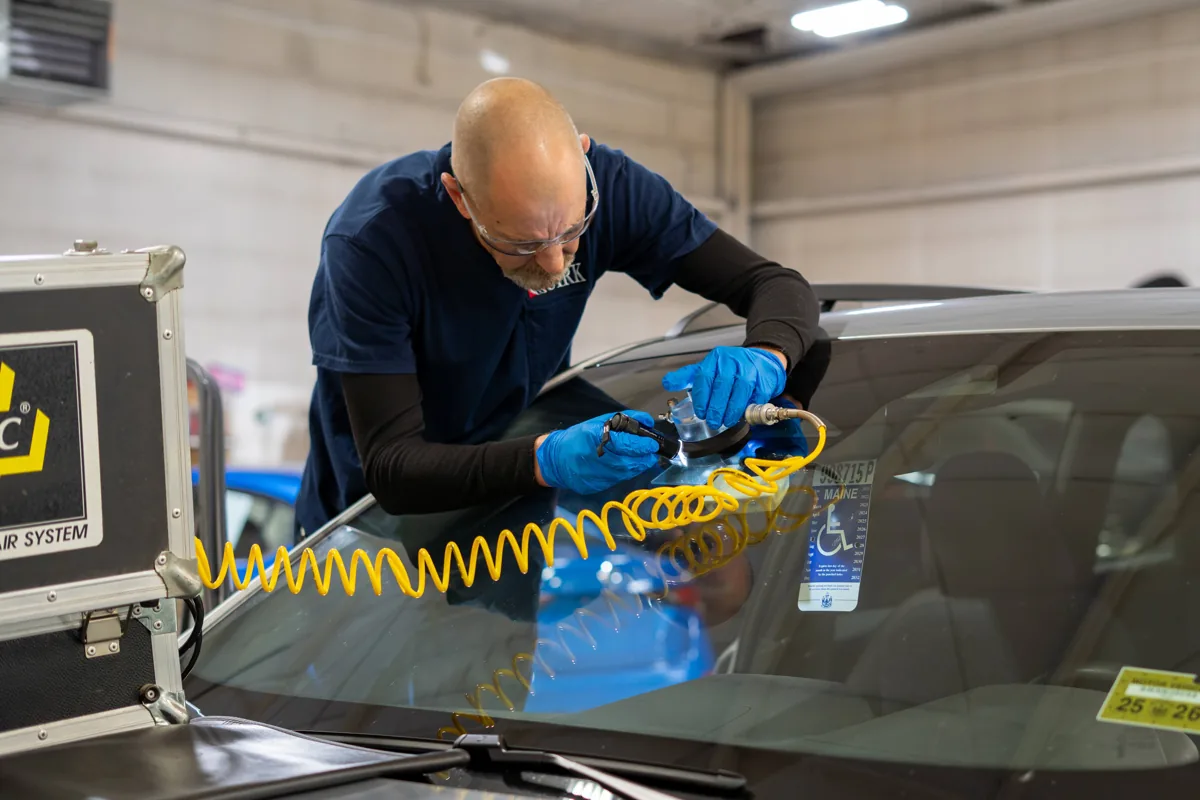 Technician using a chip repair bridge tool to repair a windshield chip