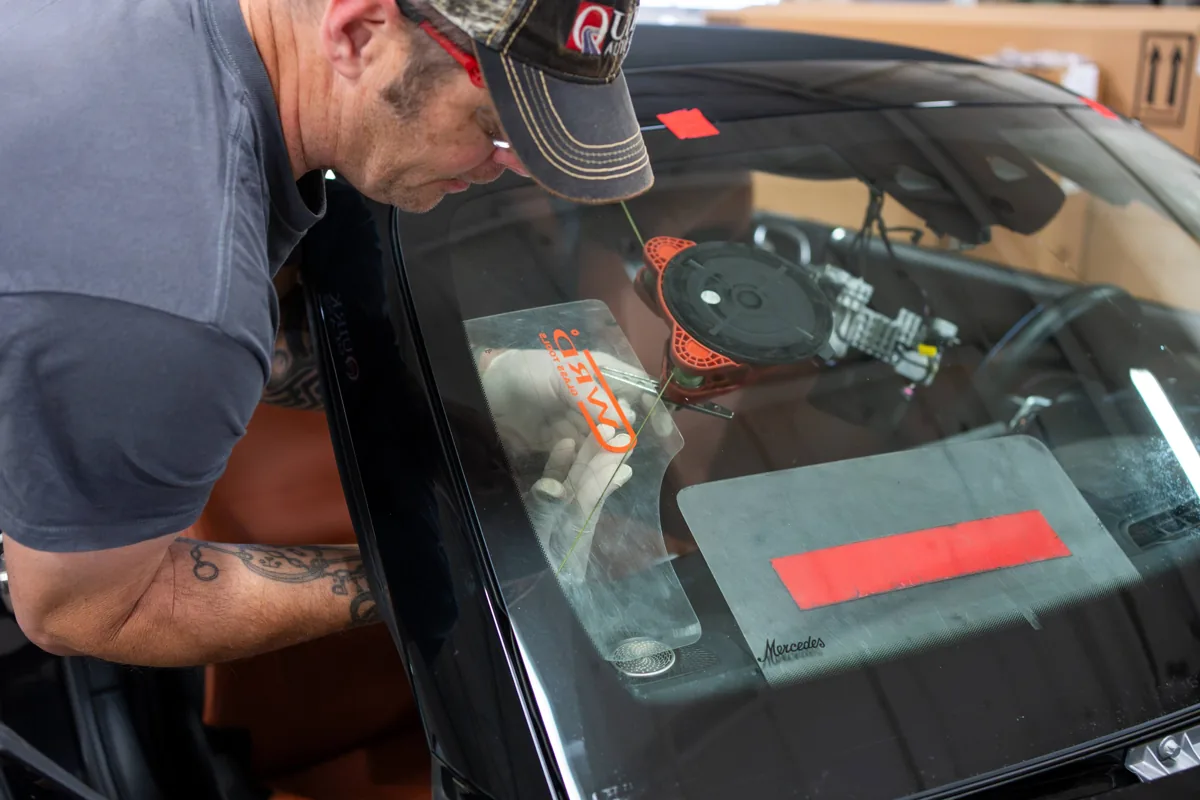 Technician applying a urethane adhesive bead to a windshield on a Mercedes